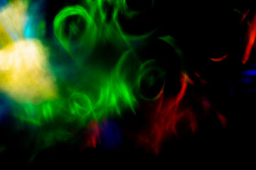 Swirling green, red, blue and yellow light forms drift across a dark background, creating an abstract motion of glowing circles, soft blur and layered luminous energy