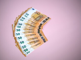 Fanned fifty euro banknotes arranged in an arc on a soft pink background, highlighting currency and financial themes.