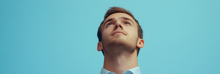 Young Man Looking Up with Hopeful Expression on Blue Background