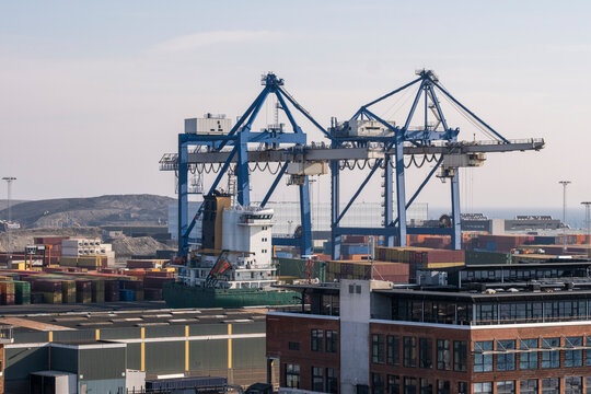 A dramatic shot of towering cranes at a busy harbor, loaded with shipping containers, representing the bustling nature of international trade and maritime logistics.