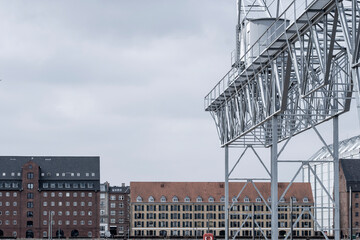 An industrial water tower frames a backdrop of historic buildings, contrasting modern functionality with timeless architecture, reflecting the evolution of urban landscapes.