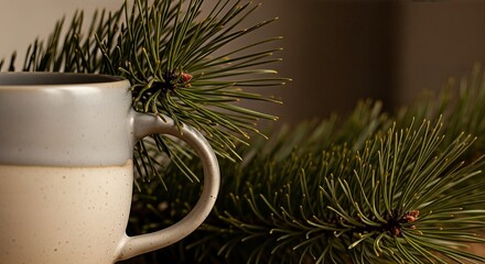 A cozy ceramic mug with a two-tone design sits next to a fresh pine branch, evoking a warm winter atmosphere.