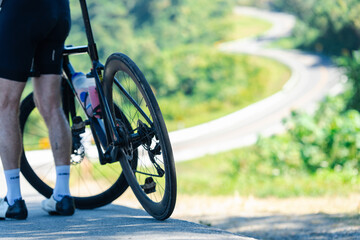 A cyclist pauses by the roadside, overlooking a winding path through lush greenery, capturing a moment of leisure and adventure in nature.