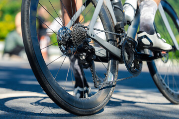 A close-up view of a bicycle wheel on a paved surface, showcasing the gears and tire, with blurred figures in the background.