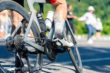 A cyclist's leg and bike in motion, capturing the essence of an active lifestyle on a sunny day, with blurred figures walking in the background.