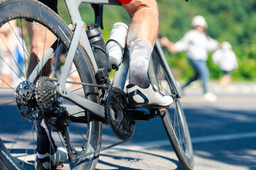 A cyclist in motion, showcasing the bicycle's gears and foot positioning, with blurred background figures emphasizing an active outdoor scene.