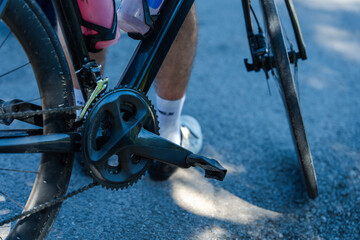 A close-up view of a cyclist's bike pedal, showcasing the gears and athlete's legs on a paved road.