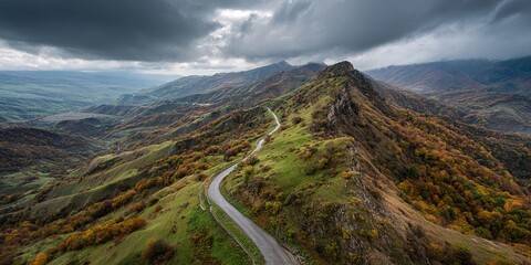 Aerial view of winding road along mountain ridge, cloudy sky, dramatic scenery, cinematic landscape