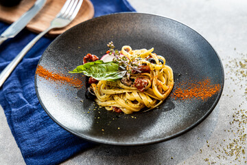 A gourmet linguine pasta dish served with sun-dried tomatoes, black olives, herbs, and basil on a black plate.