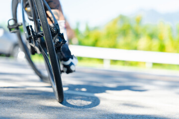 A close-up view of a cyclist"s wheel on a sunny road, showcasing the texture of the tire and the blurred background of greenery.