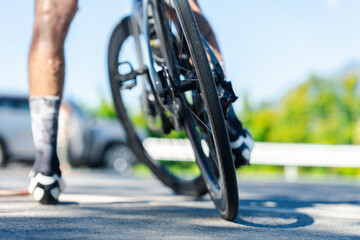 A close-up shot of a cyclist's leg and bike wheel, showcasing dynamic movement on a sunny day with blurred background elements.