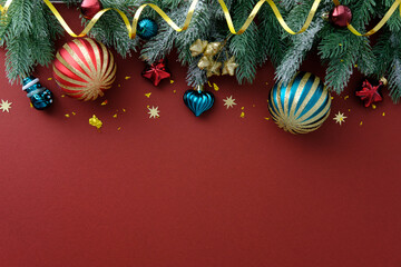 Festive Christmas border with ribbons, striped ornaments, and green frosted pine on red background.