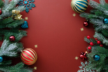 Christmas frame with snowflakes, frosted pine, red and teal ornaments on a rich red background.