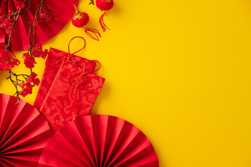 Bright yellow flat lay for Lunar New Year with red fans, red envelopes, and lanterns.