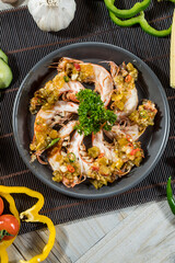 A plate of cooked shrimp arranged in a circle, topped with chili, garlic, and surrounded by fresh vegetables.