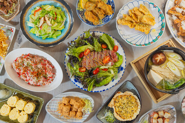 A colorful Japanese meal featuring fresh vegetables, fried items, tamagoyaki, hot pot, rice, and mochi, showcasing balance and seasonal variety.