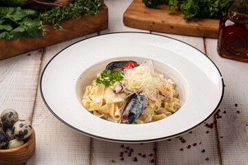 Creamy pasta with mussels, parmesan and fresh herbs served on a white plate with rustic table setting