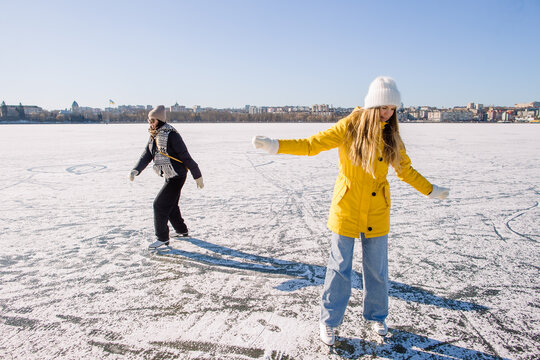 Young women ice skating on frozen lake with city background - Powered by Adobe