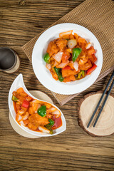 Battered chicken in sweet and sour sauce with bell peppers and onion, served in two plates on a woven placemat.