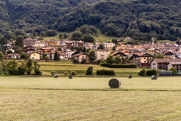 Rural alpine landscape in Pasturo, Valsassina, Italy. Idyllic view of the valley with agricultural fields and hay bales, framed by the lush mountains