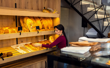 Smiling female baker arranging freshly baked bread on shelves inside bakery.