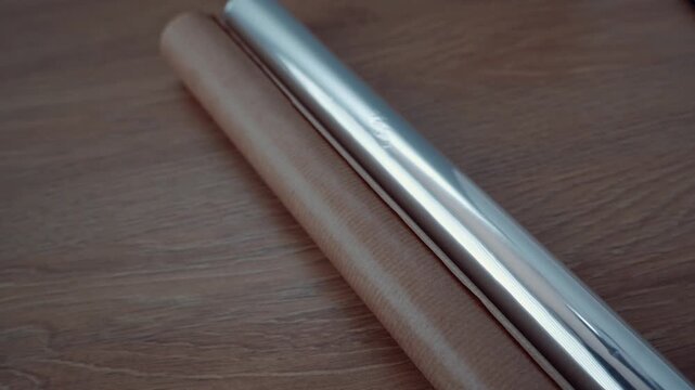 A shiny metal rolling pin is rolled over a wooden surface in a kitchen, preparing for baking dough. The focus is on the smooth motion and the reflection of light on the metal
