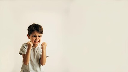 An angry young boy yells and clenches his fists, expressing strong negative emotions, frustration, and rebellion against a white background. Childhood tantrum concept