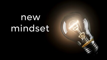 Glowing incandescent light bulb illuminates the concept of achieving a new mindset against a dark background