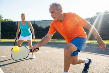 Two seniors engaged in a squash game on a sunny day at a sports facility