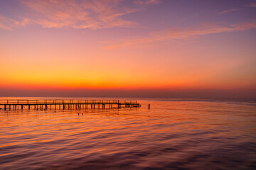 A view of the sea and sky with a wooden bridge bathed in orange light in the early morning before sunrise,Abstract old wooden bridge against the backdrop of the bright morning sunrise. 