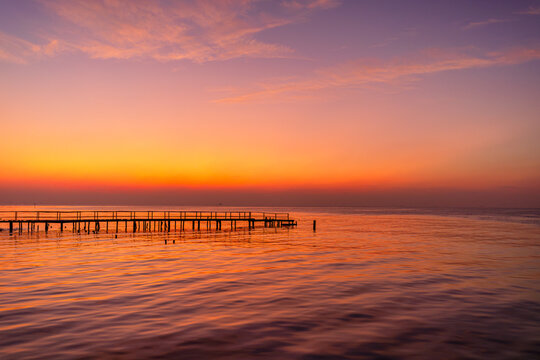 A view of the sea and sky with a wooden bridge bathed in orange light in the early morning before sunrise,Abstract old wooden bridge against the backdrop of the bright morning sunrise. - Powered by Adobe