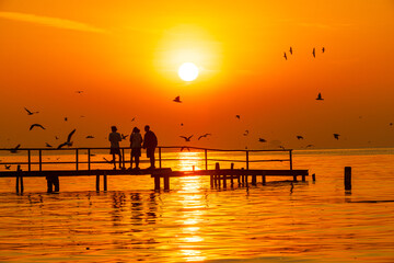 Fototapeta premium A landscape of sea and sky with a wooden bridge and tourists enjoying the orange light of the sunrise,Sunrise landscape, sea with bridge and orange sky background