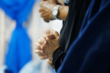 Close-up of a believer clasping their hands in prayer during worship. Soft lighting and added film...