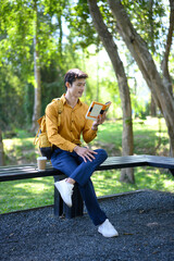 A man sits on a bench in a green park reading a book with a coffee cup