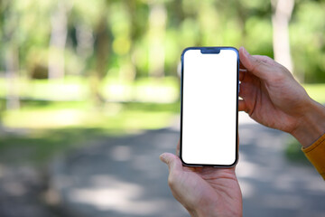 Man hand holding smartphone mockup with white screen, summer park background