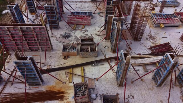 Steel structures rise against the skyline, with workers busy around concrete forms and materials scattered everywhere. Tools and machinery add to the vibrant scene of urban growth.