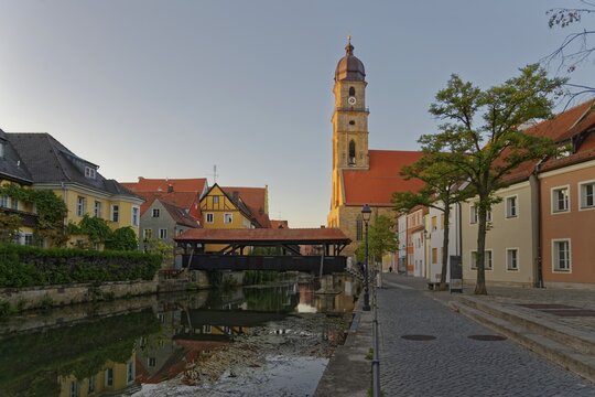 The setting sun bathes everything in warm light and reflects the Basilica of St Martin and the historic ship bridge in the River Vils, Amberg, Upper Palatinate, Bavaria, Germany