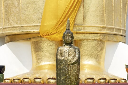 Buddha figure decorated with gold leaf in front of a 32 metre high standing Buddha statue, Wat Intharawihan, Bangkok, Thailand