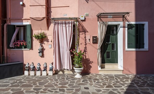 Flower pots and garden gnomes in front of pink house facade with windows and front door, colourful houses, alleys on the island of Burano, Venice, Veneto, Italy