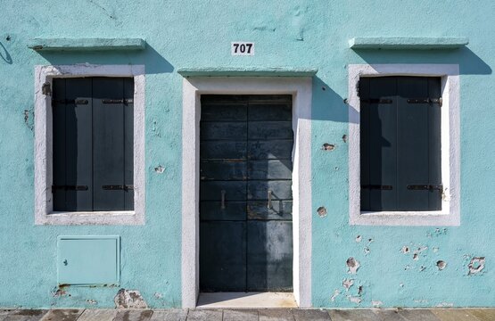 Light blue house facade with entrance door and windows with closed shutters, colourful houses on the island of Burano, Venice, Veneto, Italy