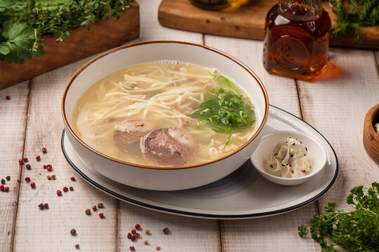 Traditional Kazakh kespe noodle soup with kazy sausage and herbs served in a bowl on rustic table