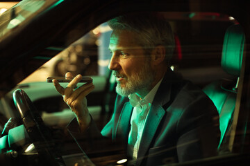 Mature man focused using smartphone voice assistant in car at night