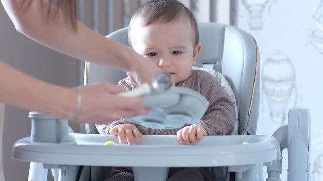 Baby Eating From Highchair, Mother Feeding, Baby Explores apple Puree With Hands While Caregiver Offers Spoon, Messy Playful Moments Under Soft