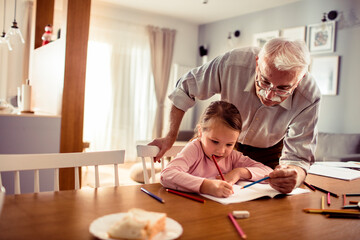 Senior grandfather teaching child granddaughter to draw at home, focused