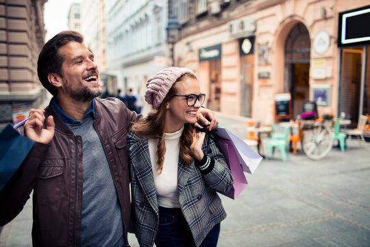 Happy young adult couple shopping together on city street