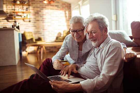 Senior couple smiling while shopping online in living room