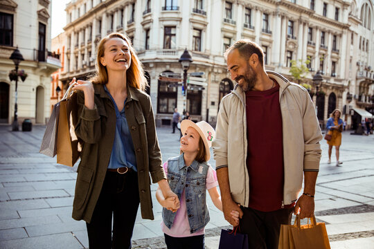 Happy adult parents and young daughter shopping in city street