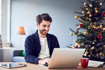 Happy young man working at home using laptop during Christmas season