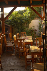 sunlit rustic patio with wooden tables and chairs, ivy covered wall and cozy bistro awaiting brunch service warm golden light