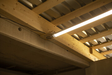Obraz premium worksite fluorescent light under wooden beams and metal decking, bright linear illumination over timber joists and temporary